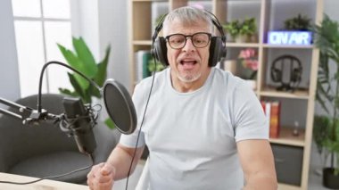 Neşeli bir son sınıf öğrencisi modern bir stüdyoda mikrofon ve kulaklıkla bir podcast kaydediyor. Mutluluk ve nişanı simgeliyor..