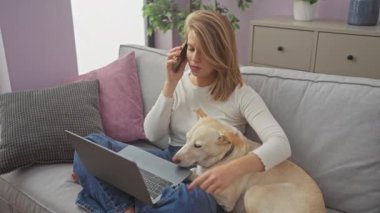 Genç bir kadın, rahat bir oturma odasında köpeğini kucağında dinlendirirken bir dizüstü bilgisayarla telefon görüşmesi yapıyor..