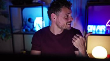 Oyun odasında video oyunu oynayan neşeli genç adam yüzünde neşeli, açık ağızlı bir gülümsemeyle baş parmağını kaldırıyor.