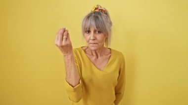 Atkuyruklu, gri saçlı, kendinden emin orta yaşlı bir kadın, izole edilmiş sarı bir fon karşısında İtalyan duygularını sert bir hareketle tasvir ediyor.