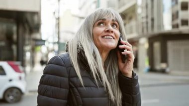 Sokak ortamında telefonla konuşan gri saçlı olgun bir kadın.