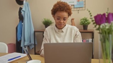 Neşeli Afro-Amerikan kadın, güzel titreşimler yayıyor, evde oturuyor, kameraya komik, mutlu bir gülümsemeyle işaret ediyor. Kapalı bir ortamda güzel bir portre.