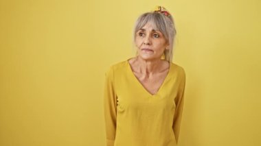 Dehşete düşmüş olgun bir kadın, gri at kuyruğu sallayarak, şaşırtıcı bir keşifle, sarı bir zemine izole edilmiş yüzüne büyük bir neşe çizer..