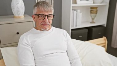 Neşeli orta yaşlı, pijamalı, kır saçlı, tamam işareti olan ve avucunda gülümseyerek, rahat yatak odasında.