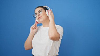 Genç ve güzel İspanyol kadın, mavi arka planda kulaklık takarak dans ediyor.