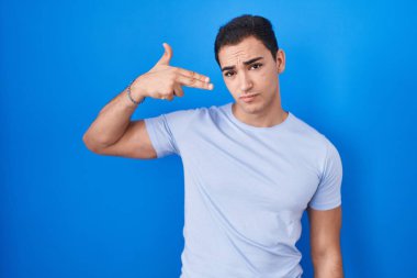 Genç İspanyol asıllı adam mavi arka planda durup kendini ve parmaklarını silah gibi havaya kaldırarak vuruyor, intihar ediyor.. 