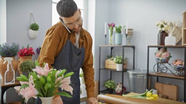 Yakışıklı İspanyol bir adam telefonda konuşurken çiçekçide zambak ayarlıyor, girişimcilik ve çoklu görev yapıyor..