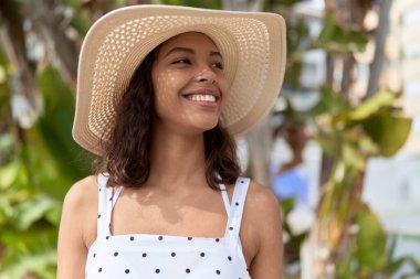 Young african american woman wearing summer hat looking to the side at park