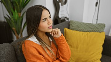 Düşünceli genç İspanyol kadın renkli yastıklı rahat bir oturma odasında dinleniyor..