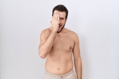 Beyaz arka plan üzerinde üstsüz duran genç İspanyol bir adam bir gözünü eliyle kapatıyor, yüzünde kendine güvenen bir gülümseme ve sürpriz bir duygu var.. 