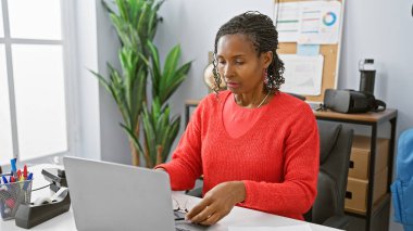 Modern ofis içinde dizüstü bilgisayarı üzerinde dikkatlice çalışan Afrikalı bir kadın..