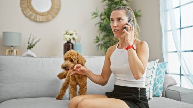 Köpekli beyaz bir kadın kanepede oturuyor ve evde telefonla konuşuyor.