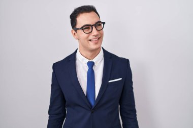 Genç İspanyol takım elbiseli ve kravatlı adam yüzünde gülümsemeyle yan yana bakıyor, doğal bir ifade. Kendinden emin gülen. 