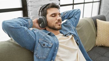 Rahat bir İspanyol adam, rahat bir oturma odasında kulaklıklarla müzik dinliyor.