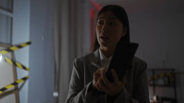 Uyarı bandıyla loş ışıklı bir odada ilginç Asyalı kadın, defterine dalgın dalgın bakıyor.