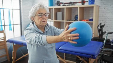 Rehabilitasyon merkezinde mavi topuyla egzersiz yapan yaşlı bir kadın..