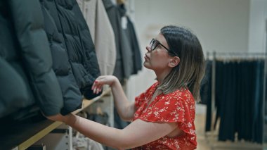 Moda tutkusu! Gözlüklü güzel İspanyol kadın perakende mağazasından şık kıyafetler seçiyor. Alışveriş merkezindeki bir butikten alışveriş yapan esmer bir kızın portresi..