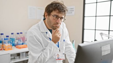 Laboratuvar önlüklü, sakallı, düşünceli genç bir adam hastane odasında bilgisayarla kafa yoruyor.