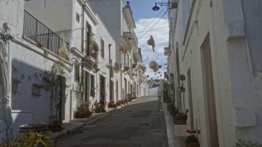 Alberobello, İtalya, Puglia 'da büyüleyici bir cadde. Asılı şapkalar, çiçekler ve mavi bir gökyüzünün altında tarihi bir şehir ortamında saksılarla süslenmiş..