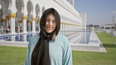 Abu dhabi camiinin beyaz mermer mimarisinin önünde tesettürlü genç ve güzel bir kadın İslami turizm ve Emirati kültürünü temsil ediyor..