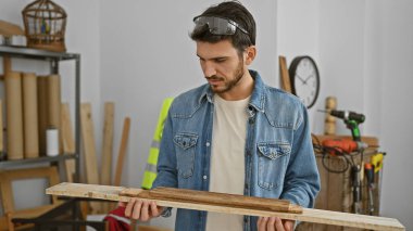 Yakışıklı bir İspanyol, iyi donanımlı bir marangozhanede ahşabı inceliyor.