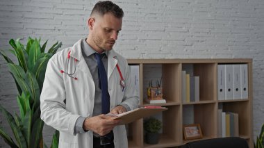 Yakışıklı İspanyol doktor bir klinikte tıbbi çizelge okuyor, sağlık sektöründe profesyonelliği ve odaklanmayı resmediyor..