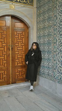 İstanbul 'daki Topkapı Sarayı' nda geleneksel Türk fayanslarının ortasında gülümseyen genç bir kadın süslü bir kapının yanında duruyor..