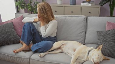 Genç bir kadın ve bir köpek, dekoratif yastıklarla rahat bir oturma odasında kanepede dinleniyorlar.