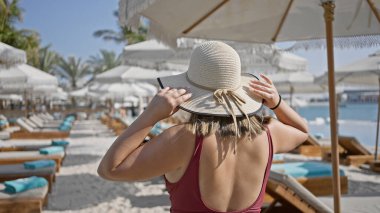 A young woman in a sundress holds her straw hat while enjoying the exclusive ambiance of a luxury poolside at a tropical resort. clipart