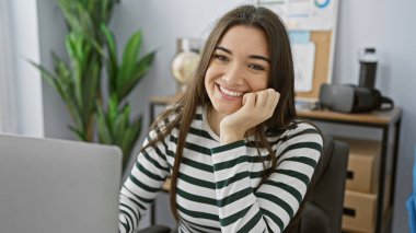 Modern bir ofiste poz veren esmer saçlı neşeli, genç bir İspanyol kadın.,