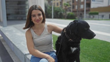 Genç, güzel bir İspanyol kadın şehir parkında siyah labrador köpeğiyle şehir merkezinde oturuyor..