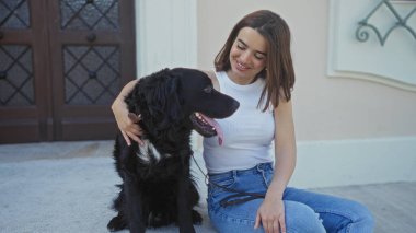 Güzel, genç bir İspanyol kadın şehir sokağında oturuyor ve gülümserken mutlu bir şekilde labrador köpeğini okşuyor..