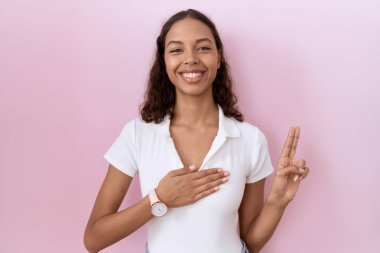 Young hispanic woman wearing casual white t shirt smiling swearing with hand on chest and fingers up, making a loyalty promise oath 