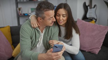 Çift, rahat, modern oturma odasında akıllı telefona bakarak eğleniyor.