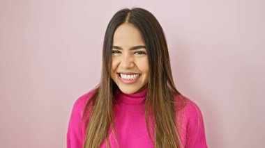 Pembe kazaklı neşeli, genç bir İspanyol kadın soyutlanmış pembe bir duvara gülümsüyor, sıcaklığını ve dostluğunu iletiyor..