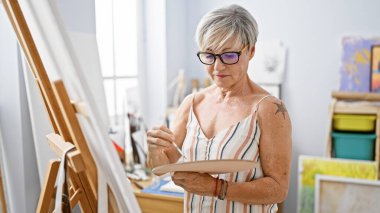 Olgun bir kadın, parlak bir sanat stüdyosunda tuvale resim çiziyor, yaratıcılık ve eğitim sergiliyor..