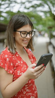 Neşeli, güzel, gözlüklü İspanyol kadın Tokyo 'nun şanslı Goşokuji Tapınağı' nda akıllı telefon kullanarak mutlu bir şekilde gülümsüyor.