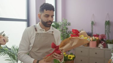 Önlüklü genç bir İspanyol çiçekçi dükkanında çiçek düzenliyor ve çiçekçilik yeteneklerini sergiliyor..