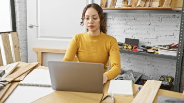 Marangozluk atölyesinde dizüstü bilgisayar kullanan odaklanmış bir kadın..
