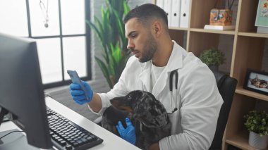 İspanyol erkek veteriner klinikte tekel köpeği tutarken cep telefonu kullanıyor..