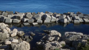 Gelibolu, puglia, salento, İtalya 'da açık mavi deniz kenarındaki beton bloklar ve kayalar güneşli bir günde insan yapımı bir dalgakıran gösteriyor..