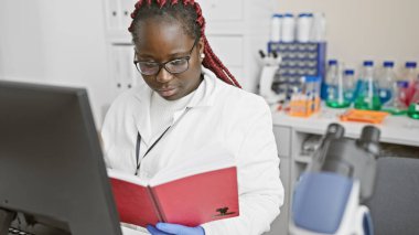 Örgü örgülü Afrikalı Amerikalı kadın bir laboratuarda kitap okuyor, araştırma, sağlık ve eğitim sergiliyor..