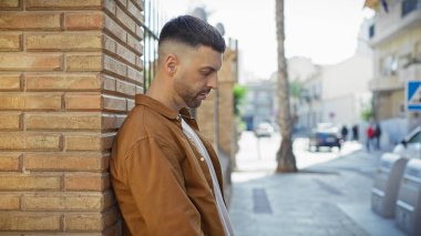 Yakışıklı, sakallı, şık bir ceketle güneşli bir şehir sokağında poz veren bir İspanyol..