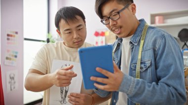 İki adam, modern bir terzide tablet üzerinde bir tasarımı analiz ediyor..