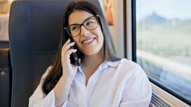 Genç ve güzel İspanyol kadın gülümsüyor. Telefonda konuşuyor. Tren vagonunda oturuyor.