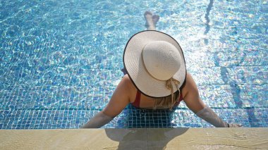 Güneş şapkalı genç bir kadın yazın köpüklü bir tatil köyünün kenarında dinleniyor..