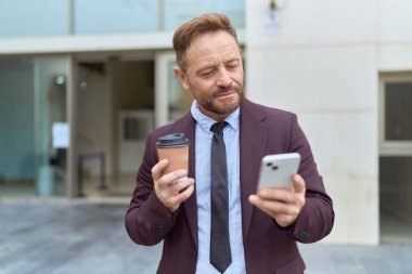 Orta yaşlı iş adamı akıllı telefon kullanıyor. Sokakta kahve içiyor.