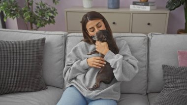 Genç bir kadın sıcak bir oturma odasında Chihuahua 'sını öpüyor, sıcaklığı ve arkadaşlığı çağrıştırıyor..