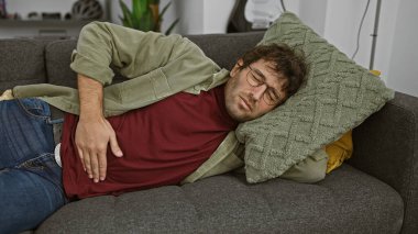 Evde kanepede yatarken karnının ağrıdığını hisseden sakallı İspanyol bir adam..