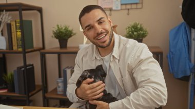 İçi rahat bir evde siyah bir dachshund tutan gülümseyen genç İspanyol adam..